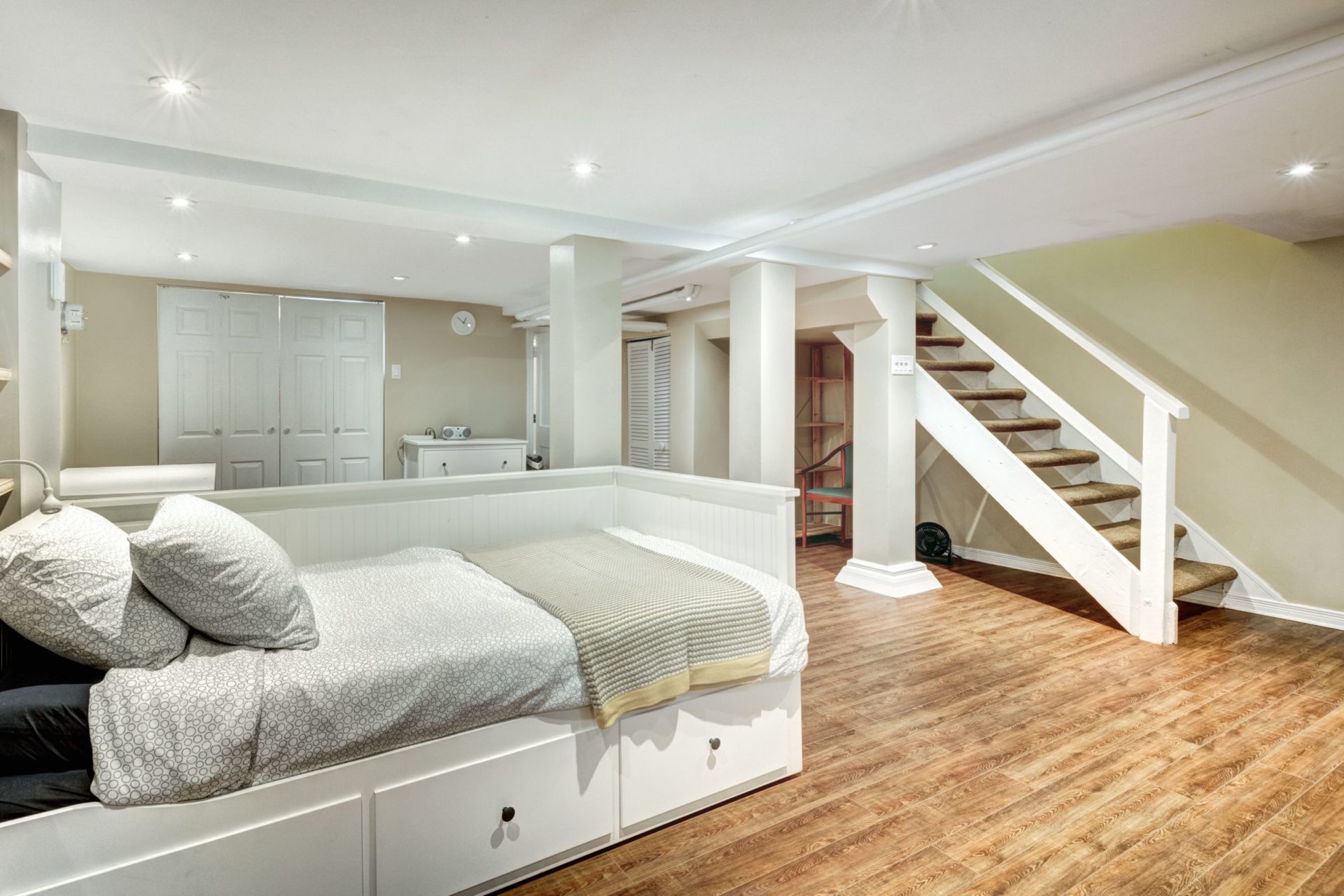 A comfortable bedroom with a bed and staircase leading upstairs. The room is well lit and has a warm atmosphere.