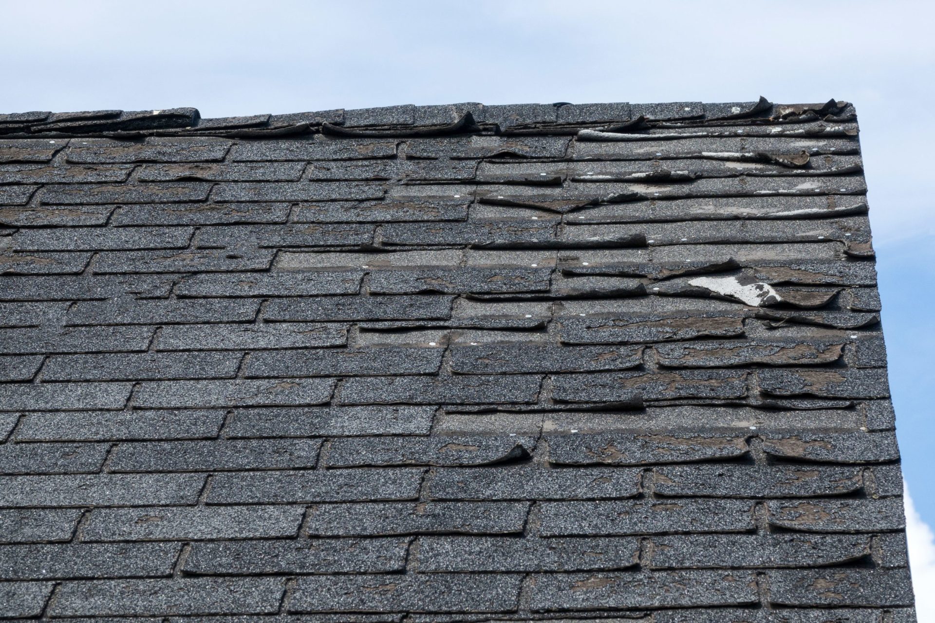 Close-up of a roof with damaged shingles. Missing shingle pieces exposed.