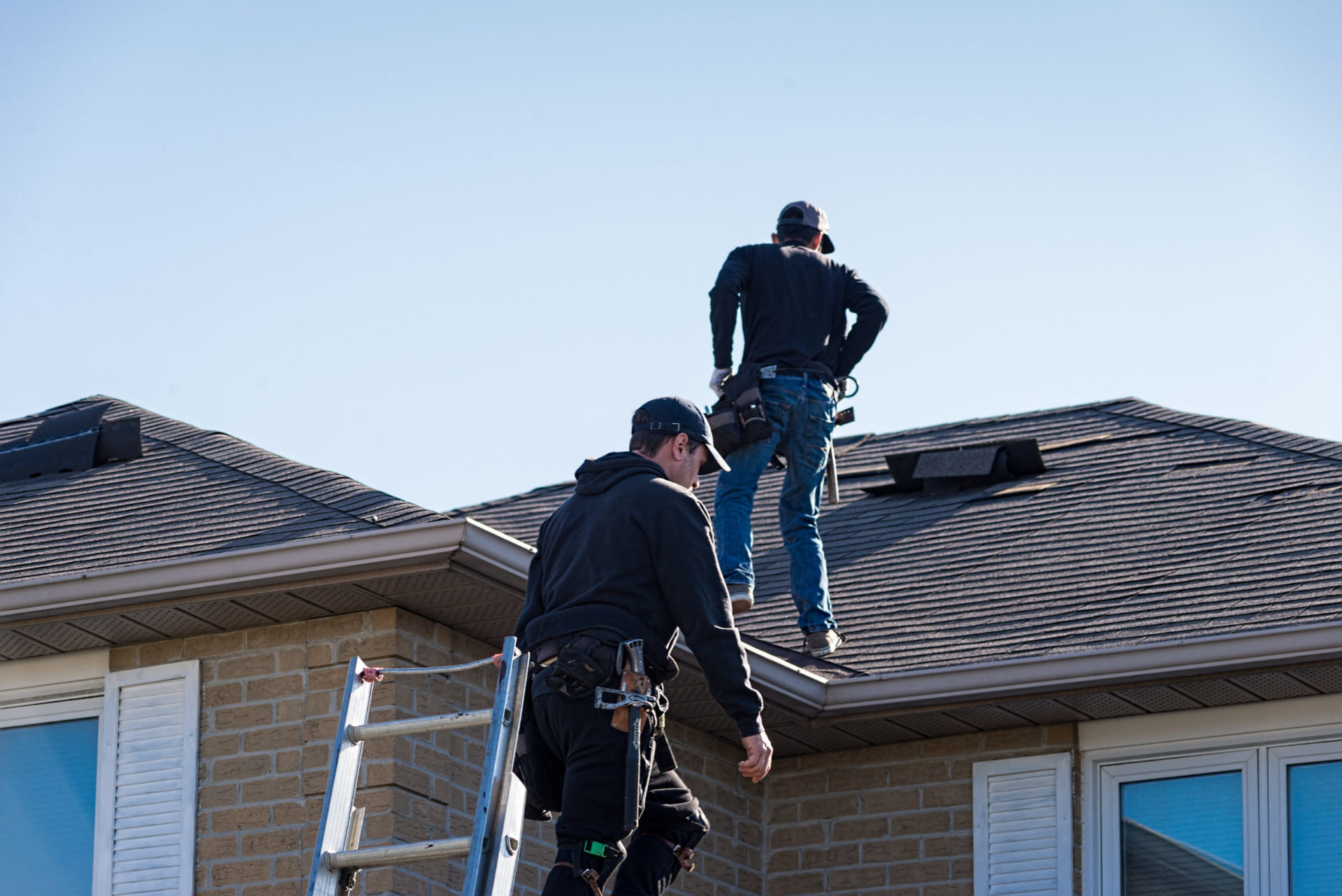 Two workers in black clothes on a roof with tools