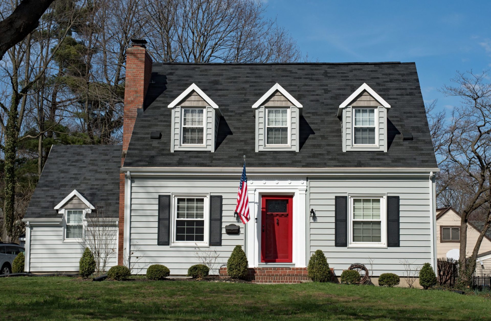 White house with red door and American flag. The house has a black roof and a brick chimney.
