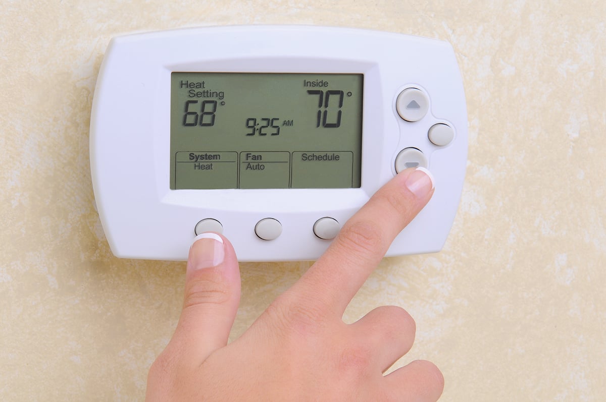 A hand adjusting a thermostat. The screen displays temperature settings.
