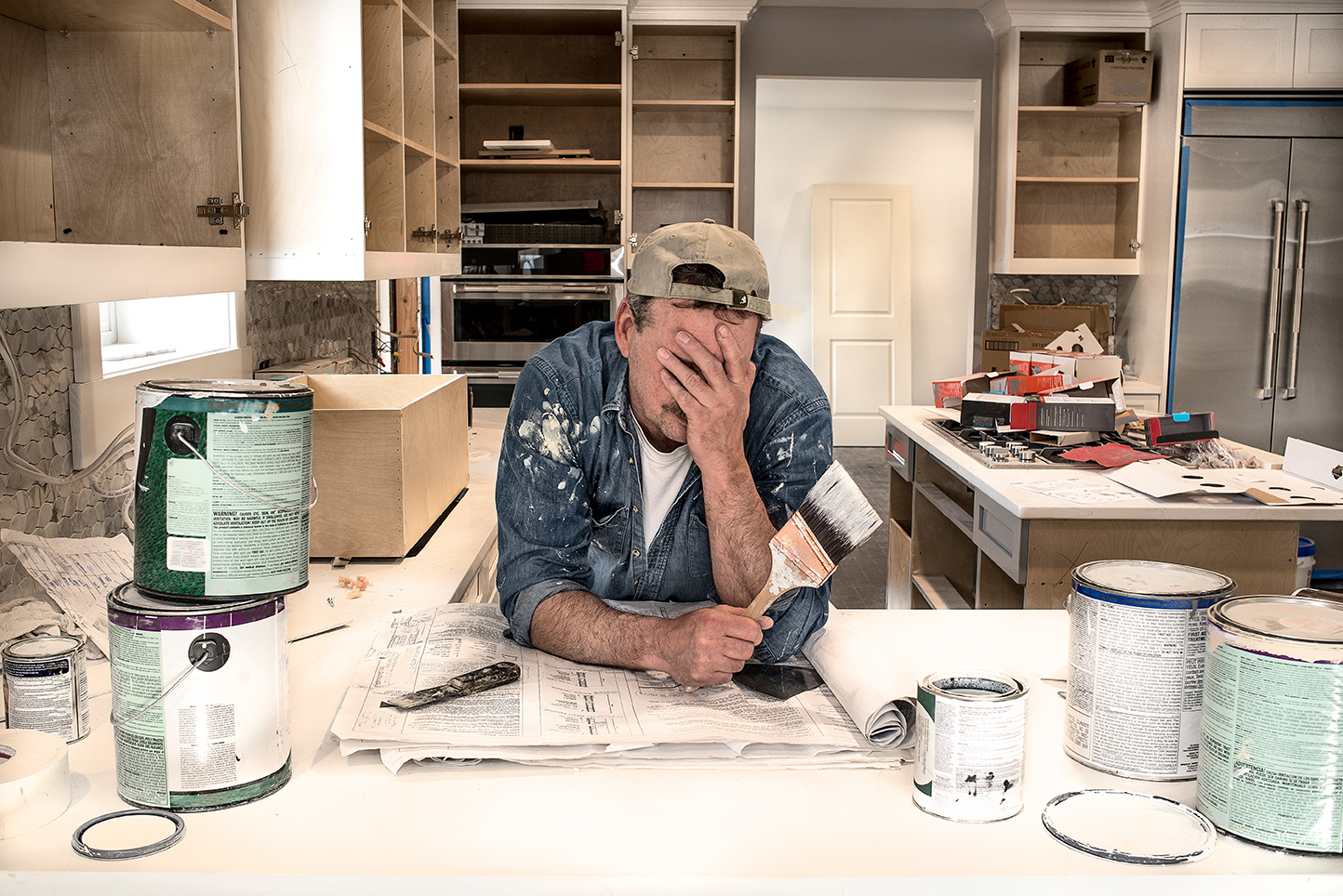 Man sitting at counter with paint cans around him. He looks stressed.