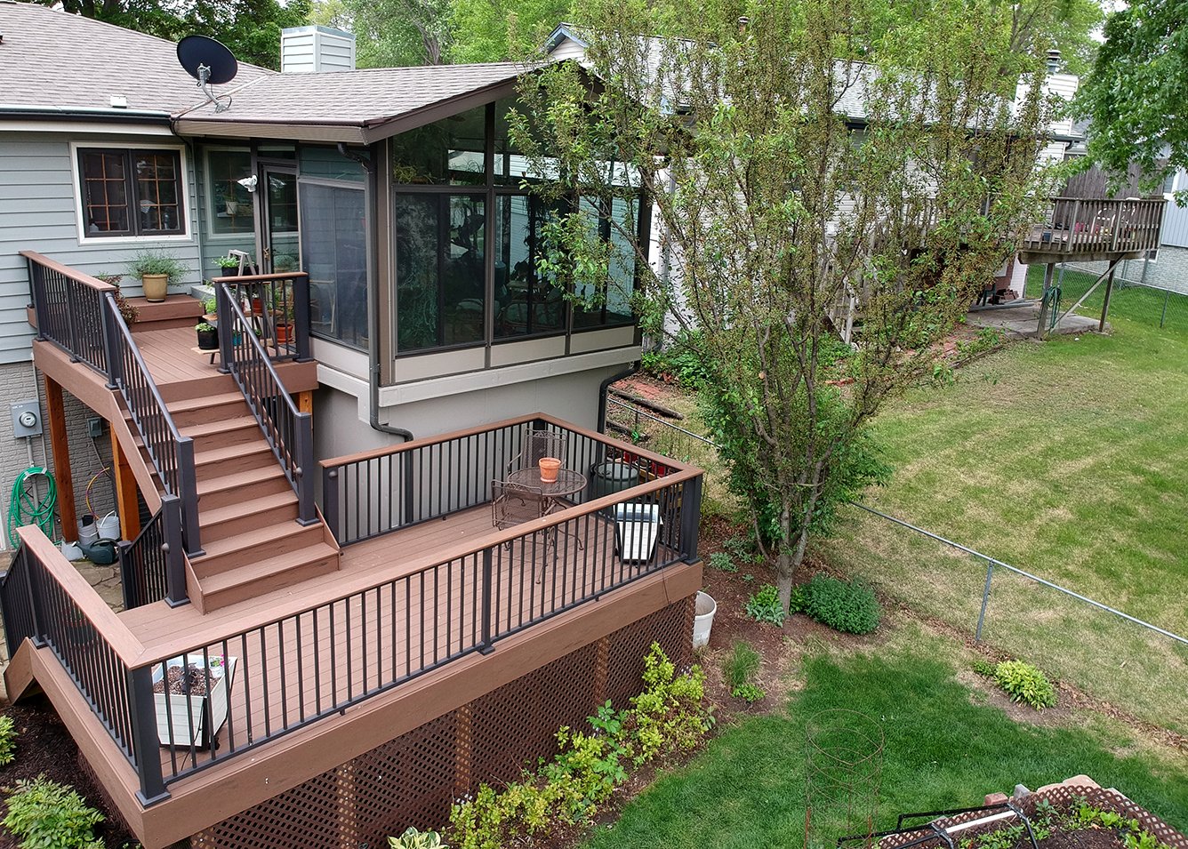 A large deck with stairs leading to a yard. The deck has black railings and brown wood.