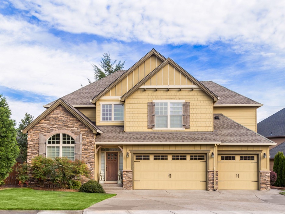 A large two-story house with a tan exterior and brown trim. The house features a two-car garage.