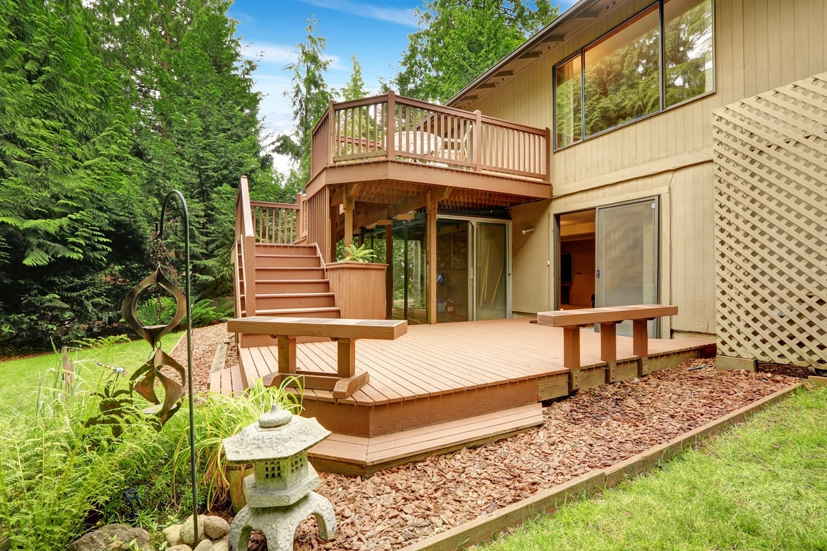 A house with a wooden deck and patio area. The deck has a staircase and a railing.