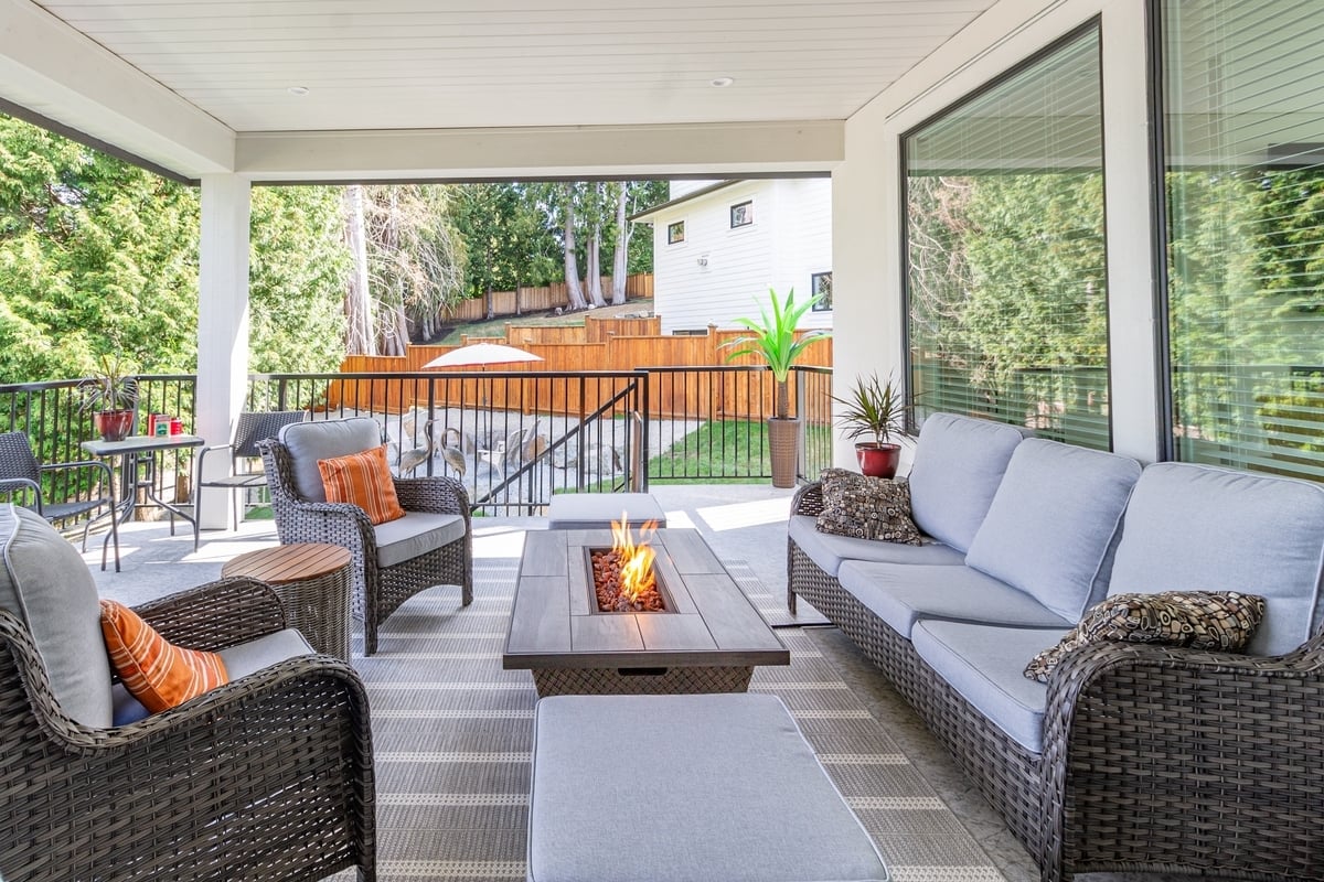 Outdoor patio with wicker furniture and fire table. Comfortable seating area with a couch and chairs.