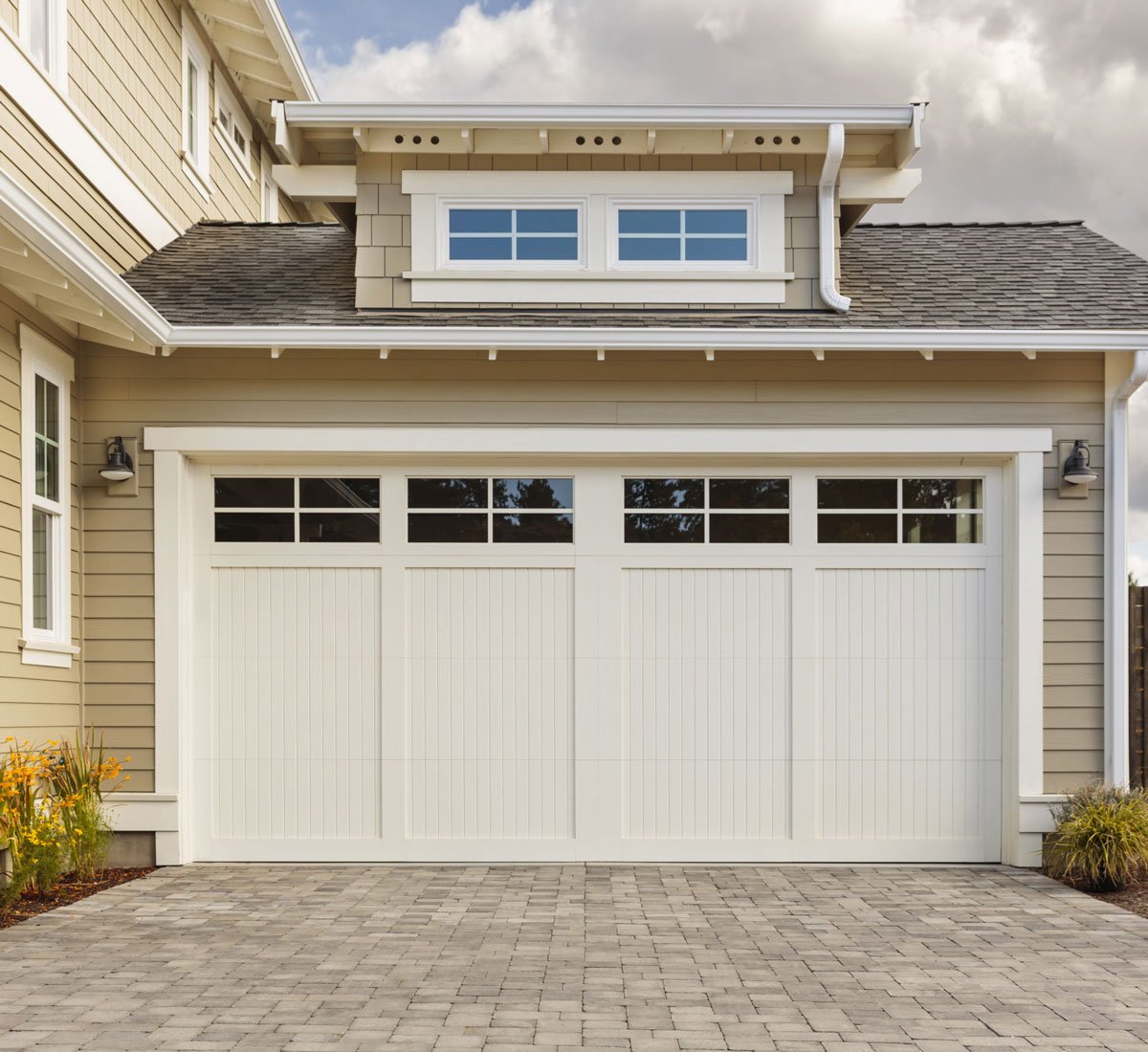 A white garage door with windows on a beige house. The garage has a brick driveway.