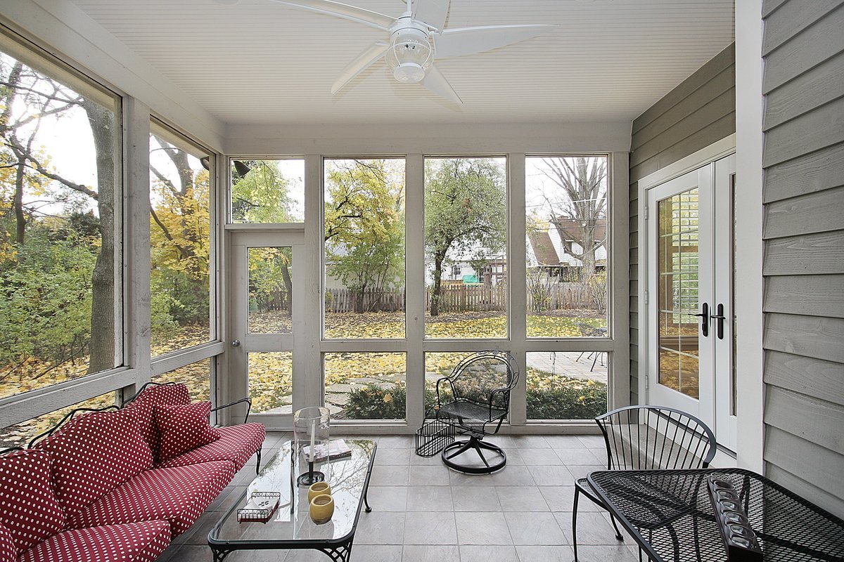 A screened-in porch with a red couch and black chairs.