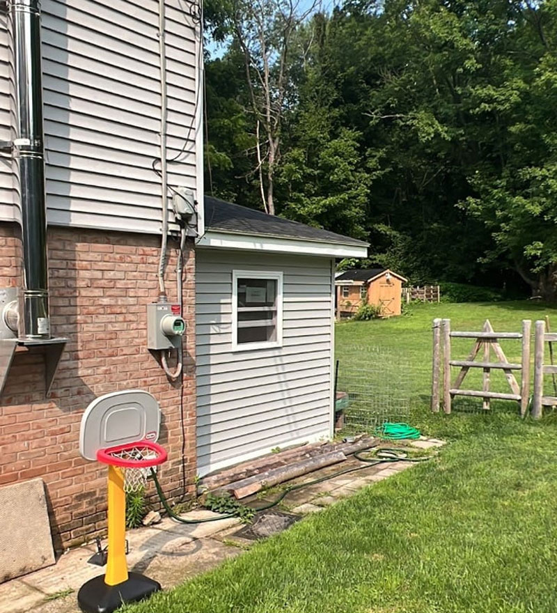 A house with gray siding and a brick base. A small basketball hoop sits on the lawn.