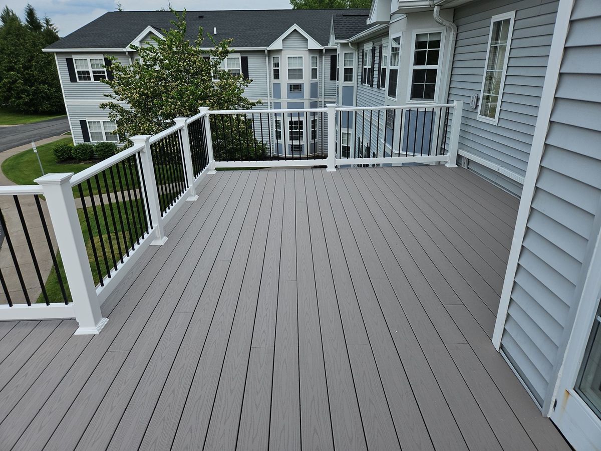 A gray deck with white railings and black balusters on a house. The deck is attached to a gray house.