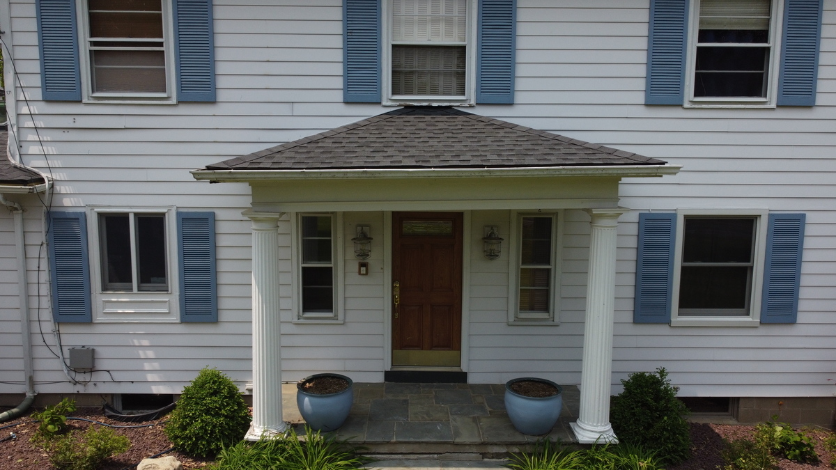 A house with a covered porch and blue planters. The house has white siding and blue shutters.