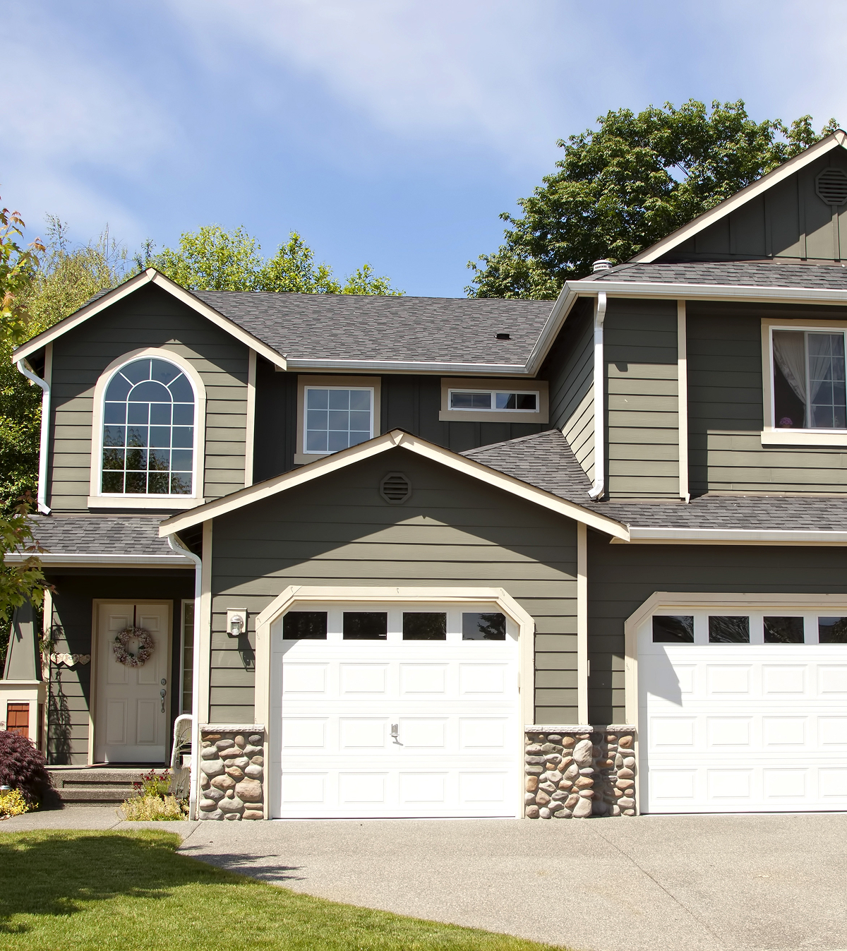 Modern Two Story House with Green Siding A two-story house with green siding and white garage doors. The house features a large arched window above the front door.