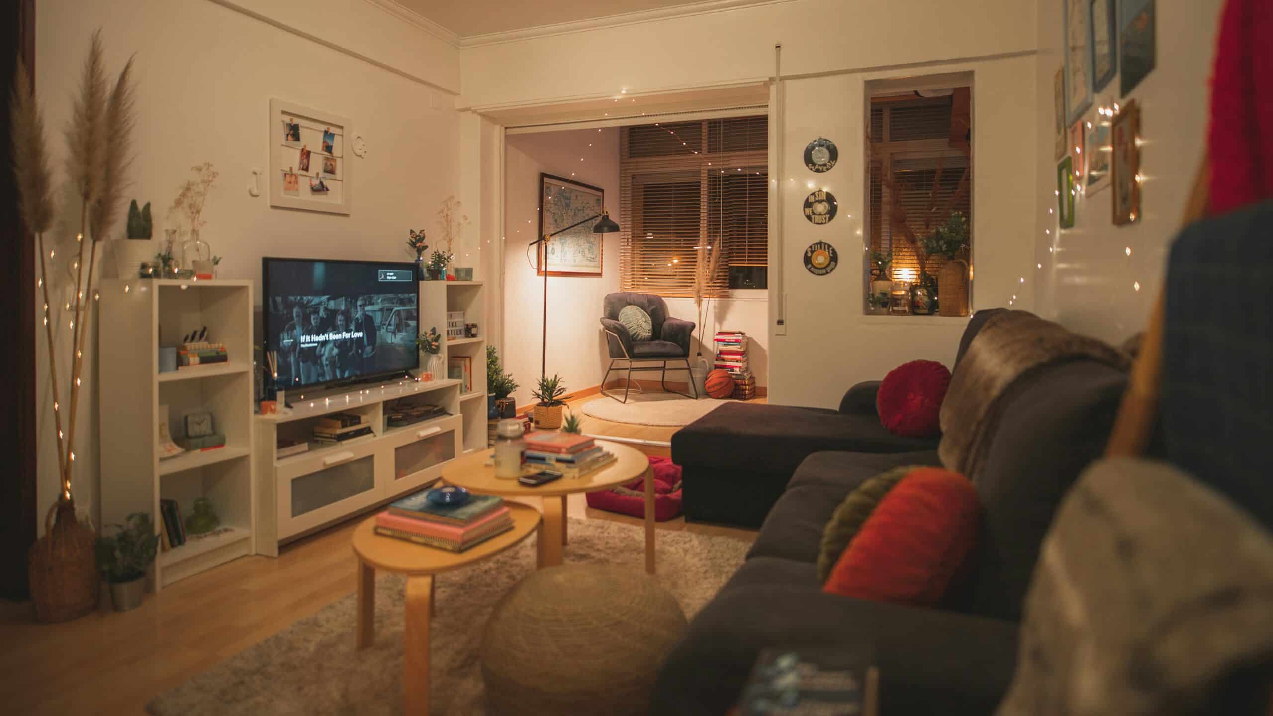 A living room with a dark couch, coffee table, and TV on a white stand. The room is well-lit and decorated with various items.