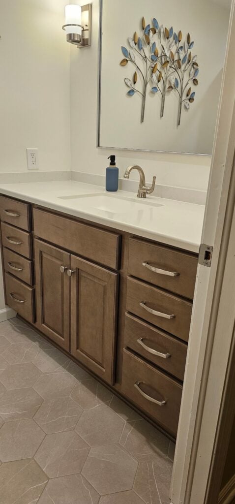 Bathroom vanity with large mirror, white countertop and brown cabinets. The sink and faucet are visible.