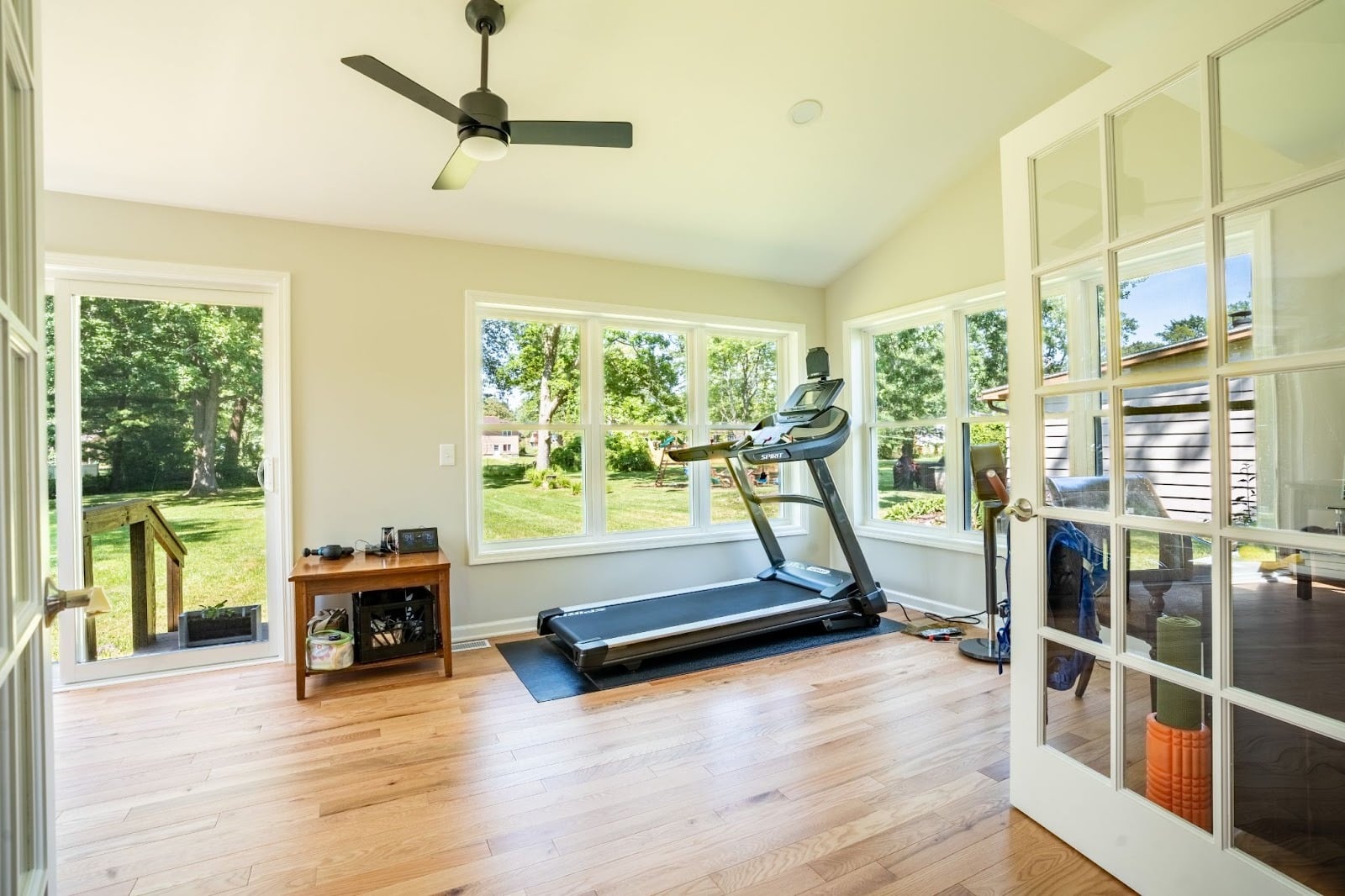 A home gym with a treadmill and exercise equipment. The room has large windows with a view of the outdoors.
