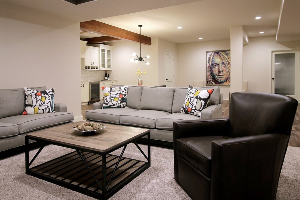 A modern living room with a gray couch and a brown leather chair. The room is well lit and has a coffee table in the center.