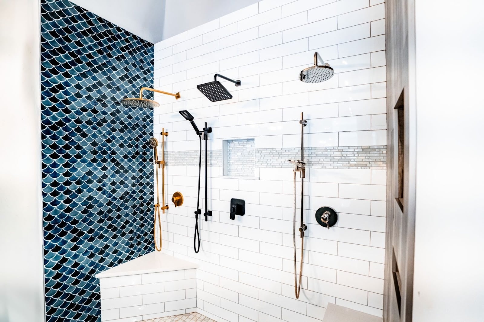 A modern bathroom shower with a blue tile accent wall and white subway tiles. The shower features gold fixtures and a rainfall showerhead.