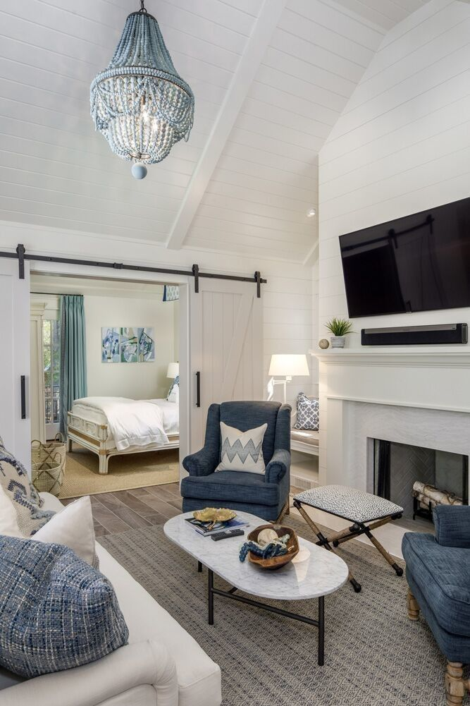 A cozy living room with a fireplace and a view of a bedroom through a sliding barn door. The room features a blue and white color scheme with comfortable furniture.