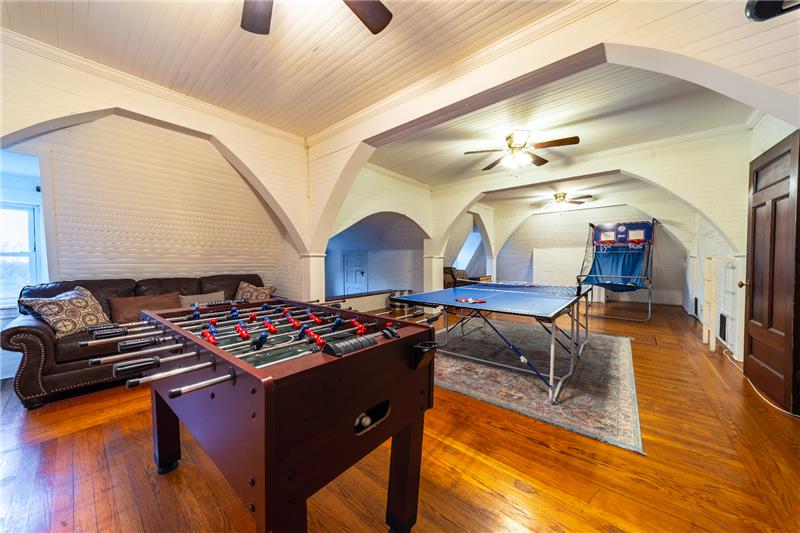 Game room with foosball table, arcade machine, and seating area. Recreational space with wooden floor.