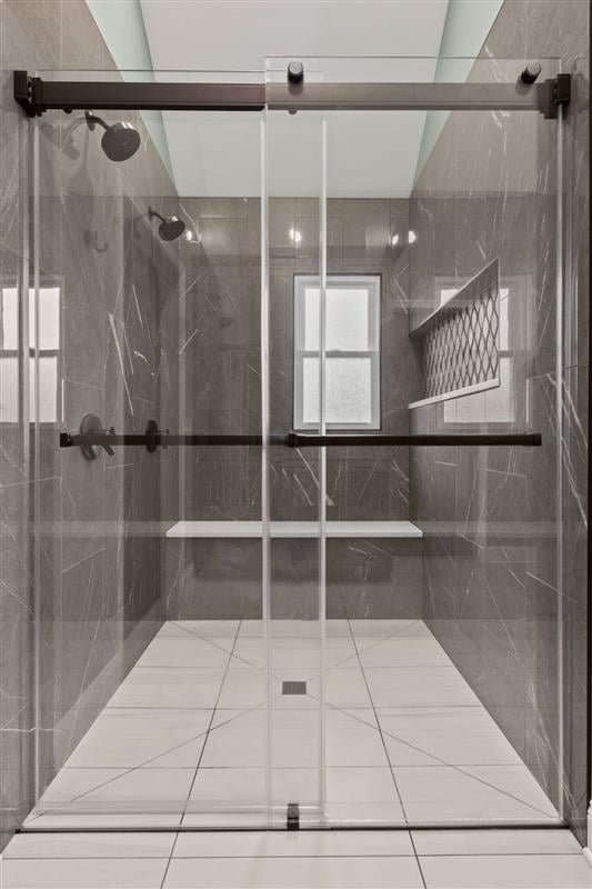 A sleek glass-enclosed shower with gray walls and white tile floor. Modern bathroom interior.