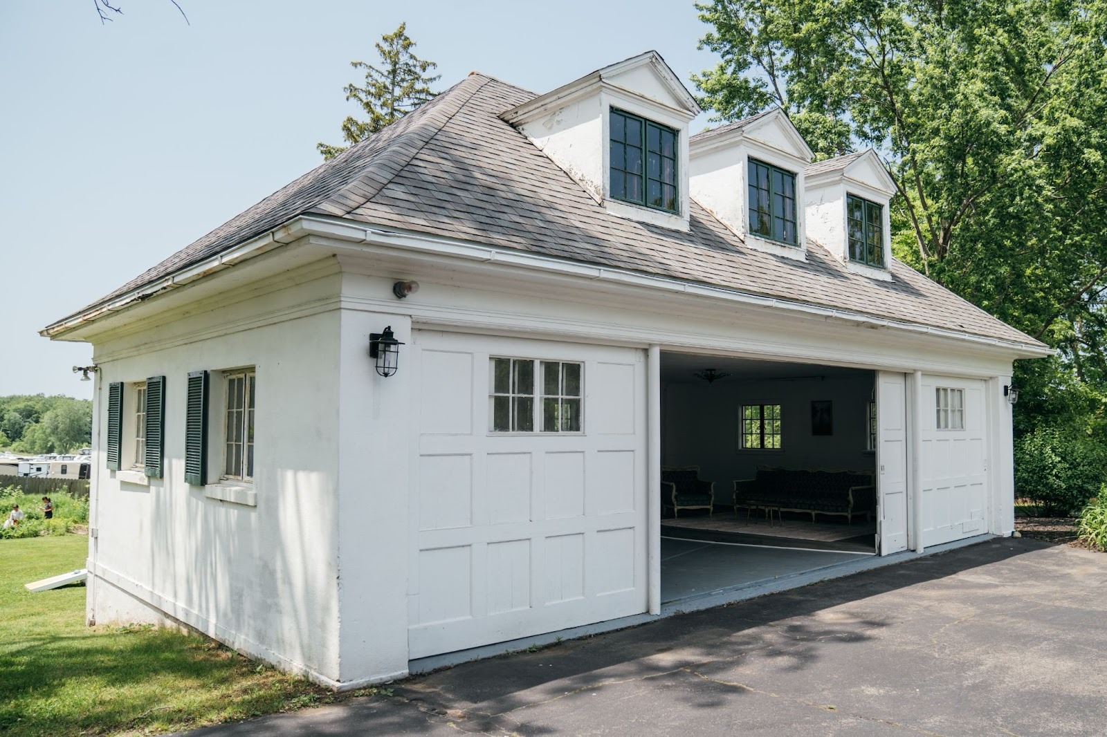 A white garage with an open door on a driveway. The garage has a gray roof and a paved driveway.