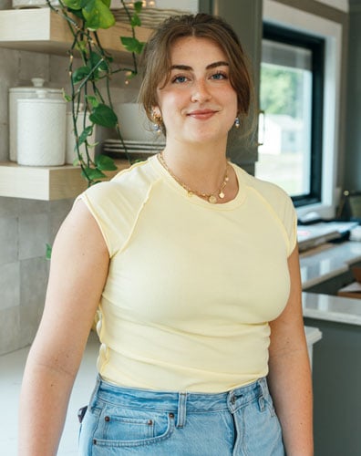A young woman wearing a yellow shirt and jeans in a kitchen
