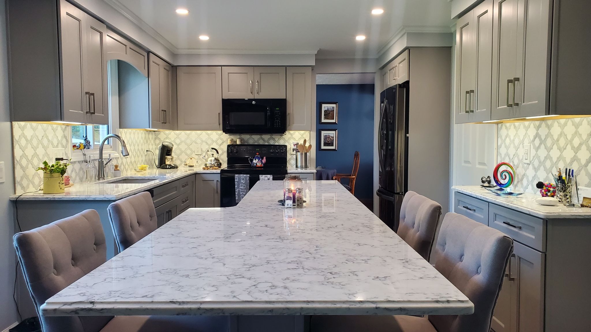 Large kitchen island with marble countertop and seating. Modern kitchen with gray cabinets and white marble backsplash.