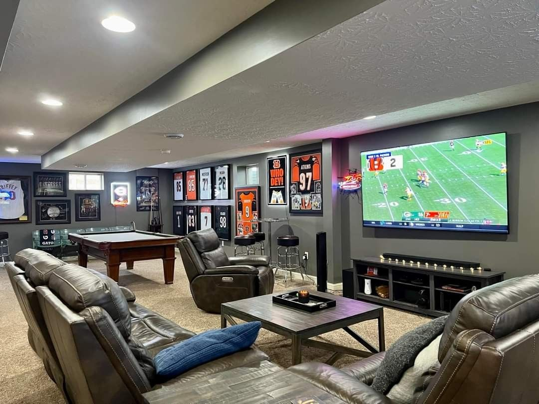 A sports-themed room with a pool table and large screen TV showing a football game. Comfortable seating area with leather couches.