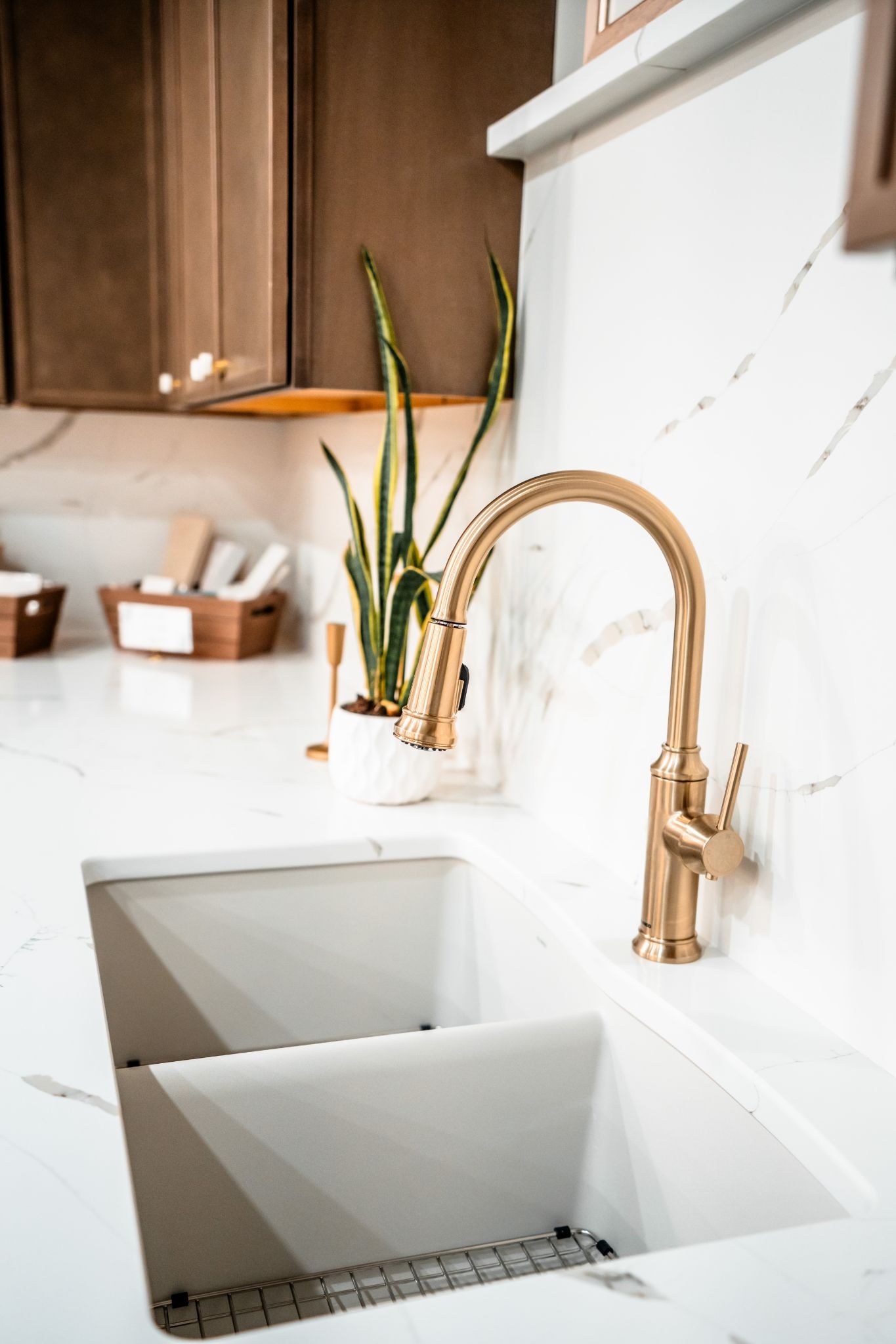 A modern kitchen sink with a gold faucet and white marble countertop. The sink is clean and empty.