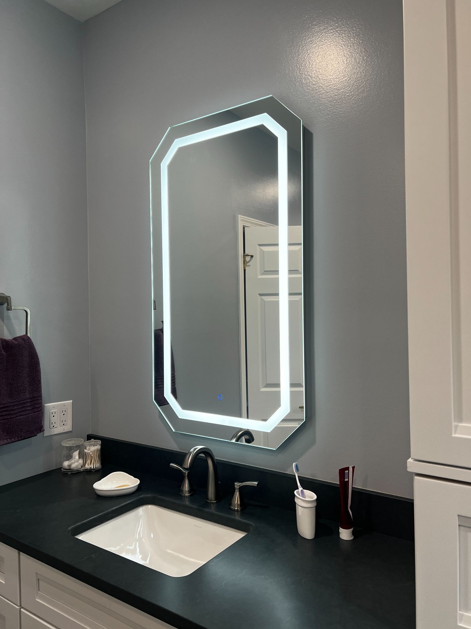 A bathroom sink with a large LED lighted mirror above it. The mirror has a white light around its edges.