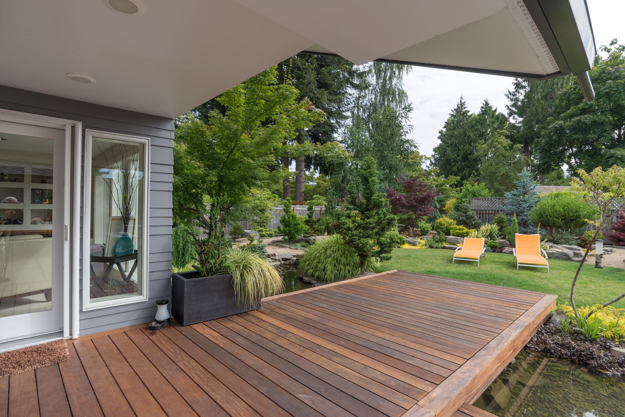 A wooden deck with a glass door leading to a garden with orange chairs.