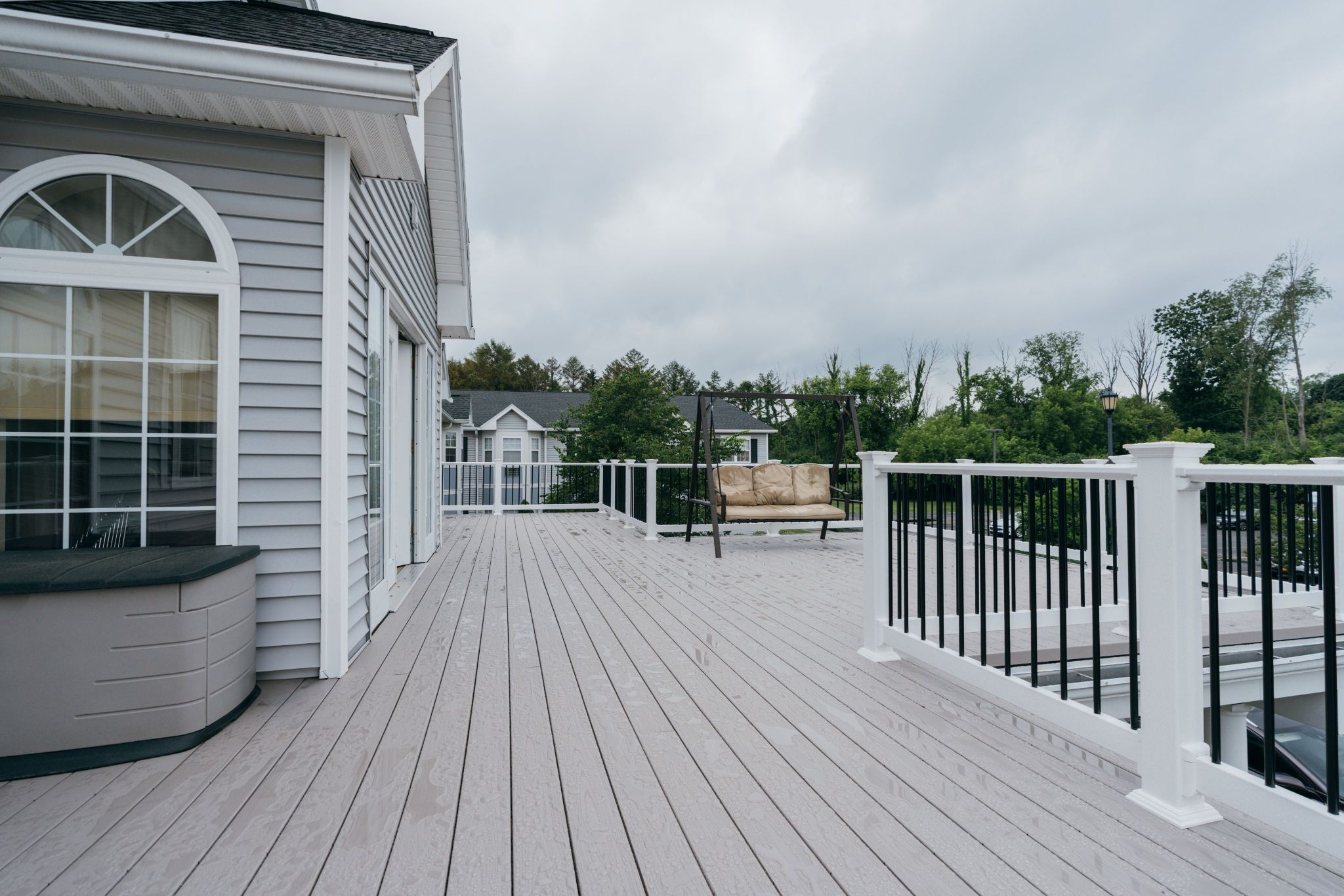 A large deck on a house with a railing. The deck is attached to a gray house.