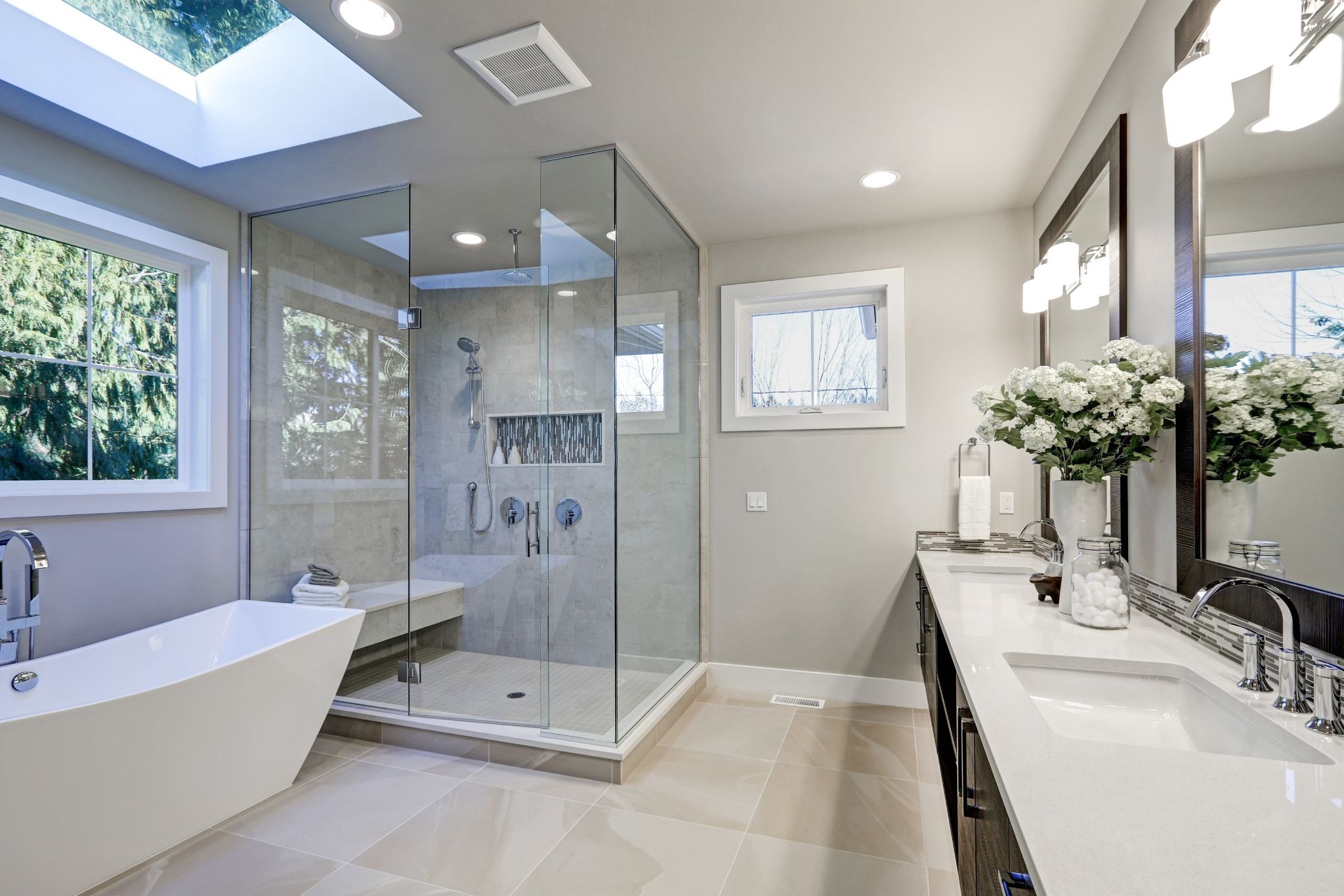 Modern bathroom interior with a freestanding tub and glass shower. A large vanity with flowers is also visible.