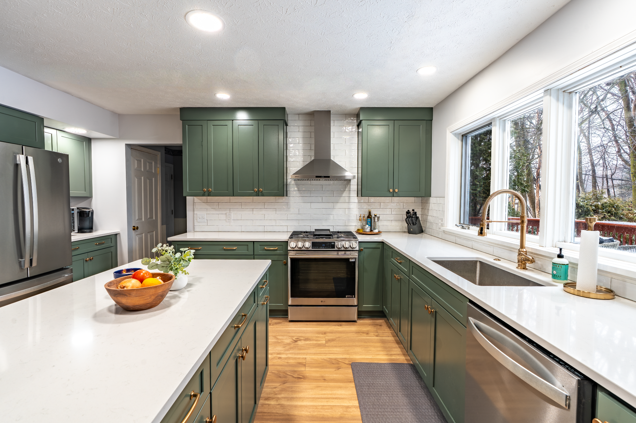 Green kitchen cabinets and white countertops with fruit bowl.