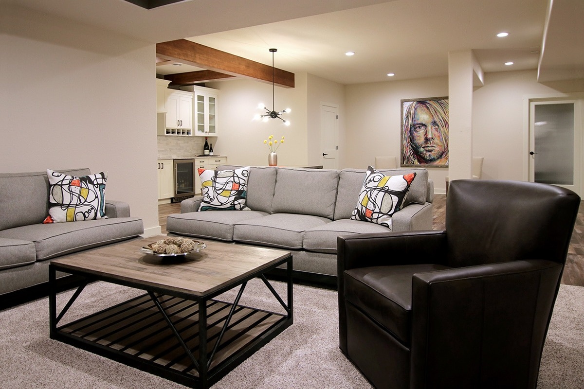 A modern living room with a gray couch and a brown leather armchair. The room is well-lit and features a coffee table.