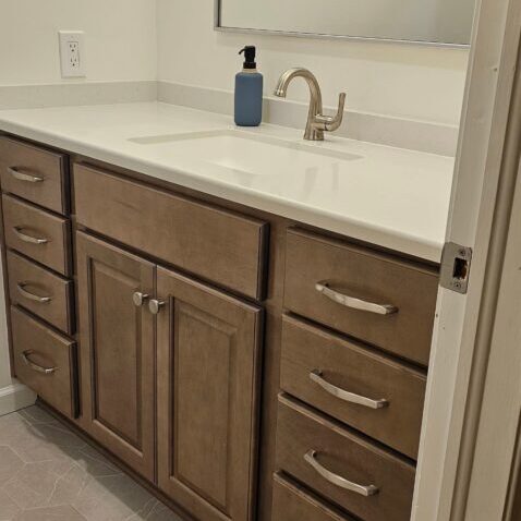 Bathroom vanity with large mirror, white countertop and brown cabinets. The sink and faucet are visible.