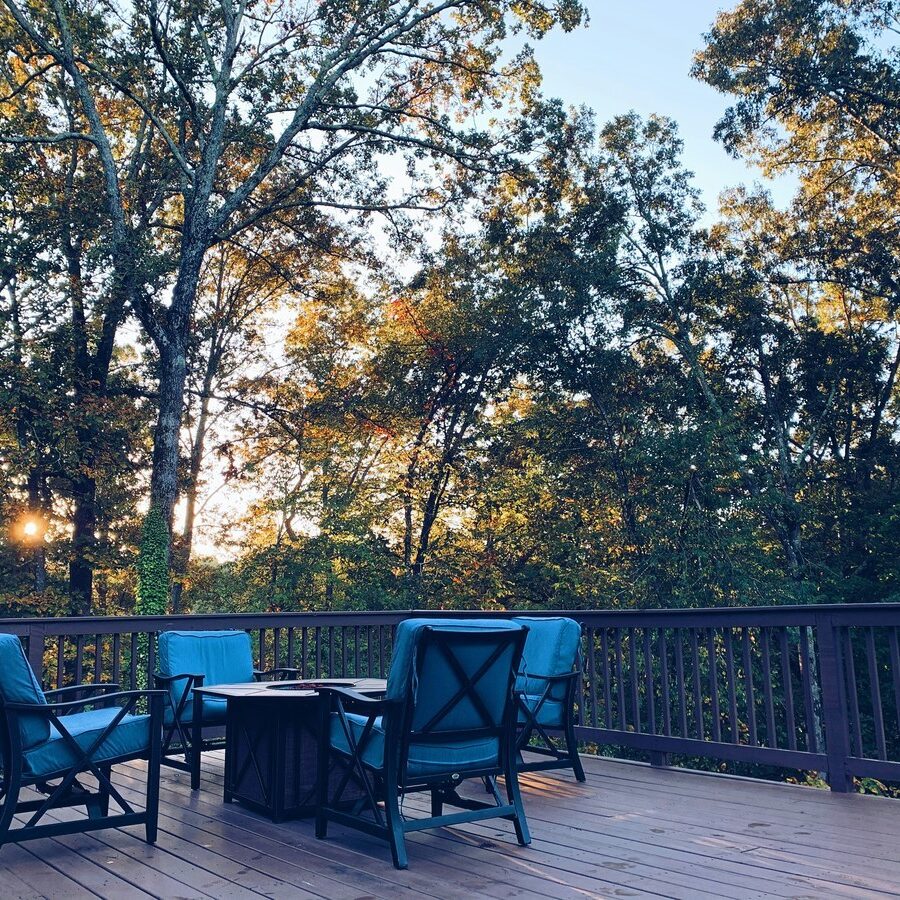 A deck with blue chairs and a table. Forest background.