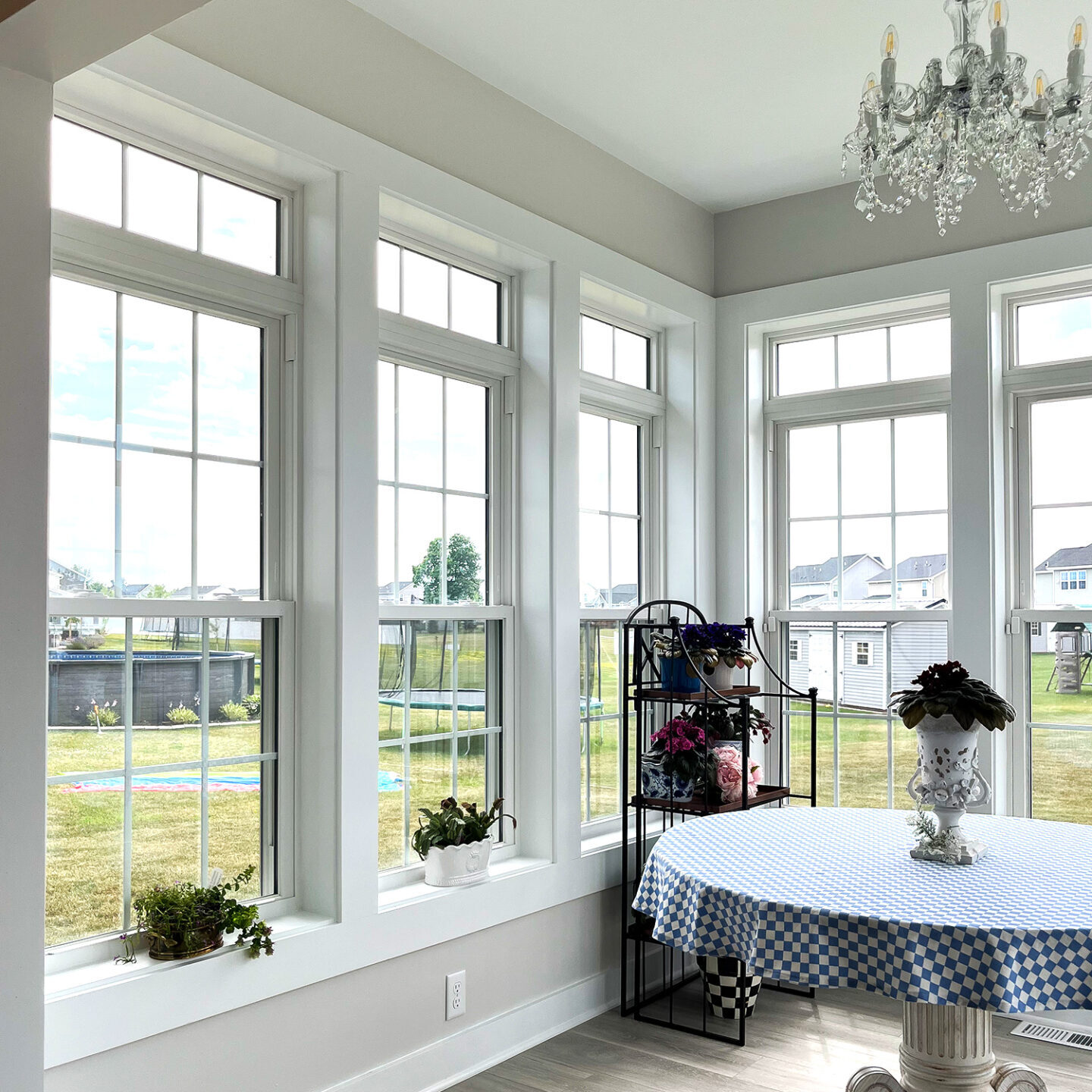 A bright dining room with large windows and a chandelier. The room has a table with a blue and white checkered tablecloth.