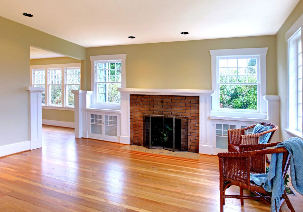 A room with a fireplace and windows. Wooden chairs sit in the foreground.