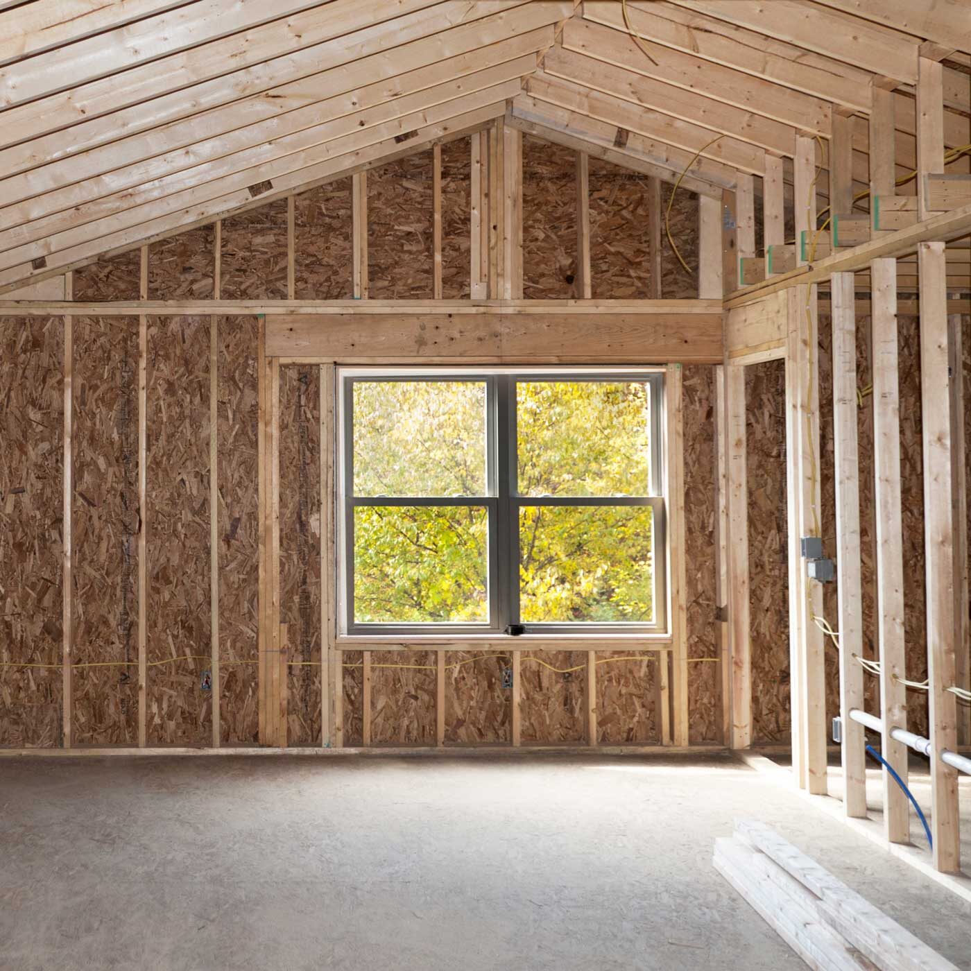 An unfinished room with a large window showing trees outside. The interior is made of wood and has a vaulted ceiling.