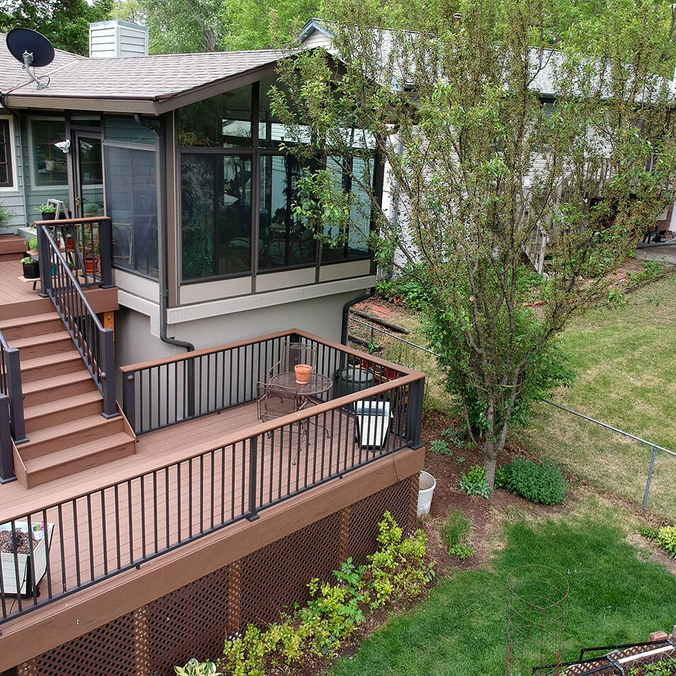 A house with a large deck and sunroom. The deck has black railings and brown wood.