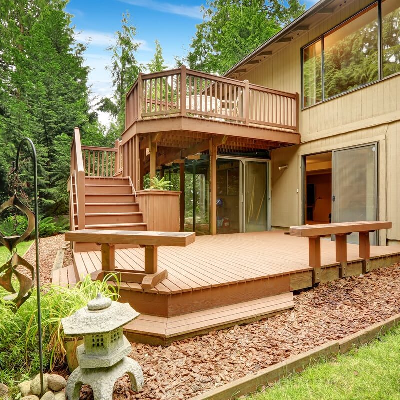 A house with a wooden deck and patio area. The deck has a staircase and a railing.
