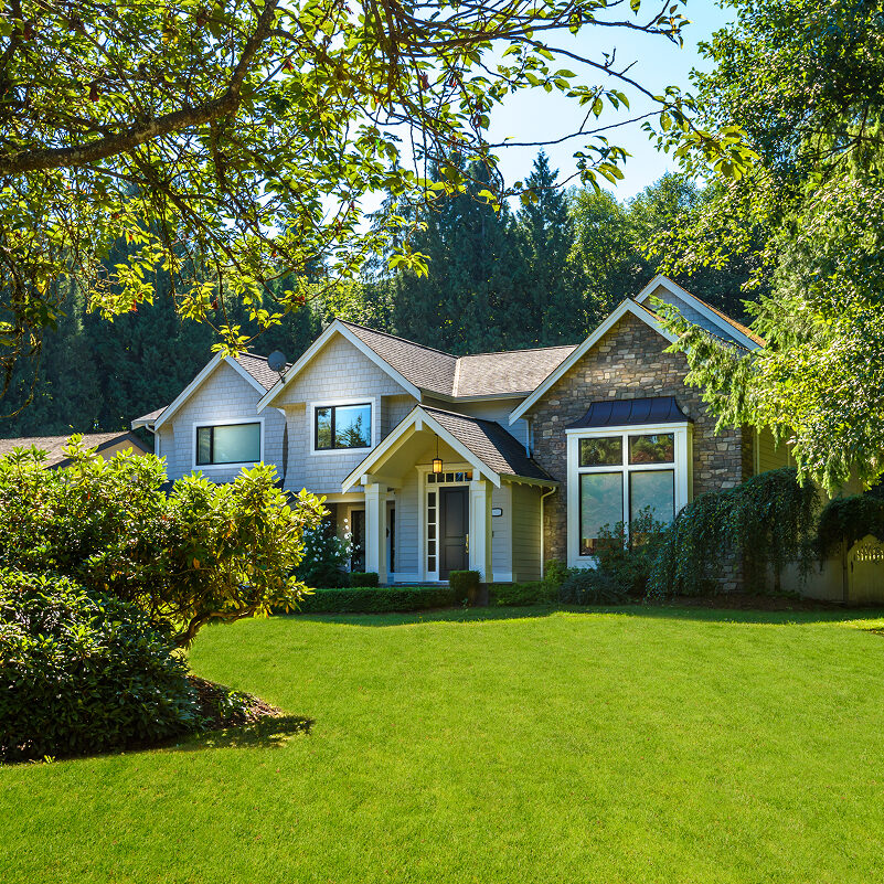 Beautiful house with large green lawn and trees A large house with a well-manicured lawn and trees. The house has a gray exterior with white trim.