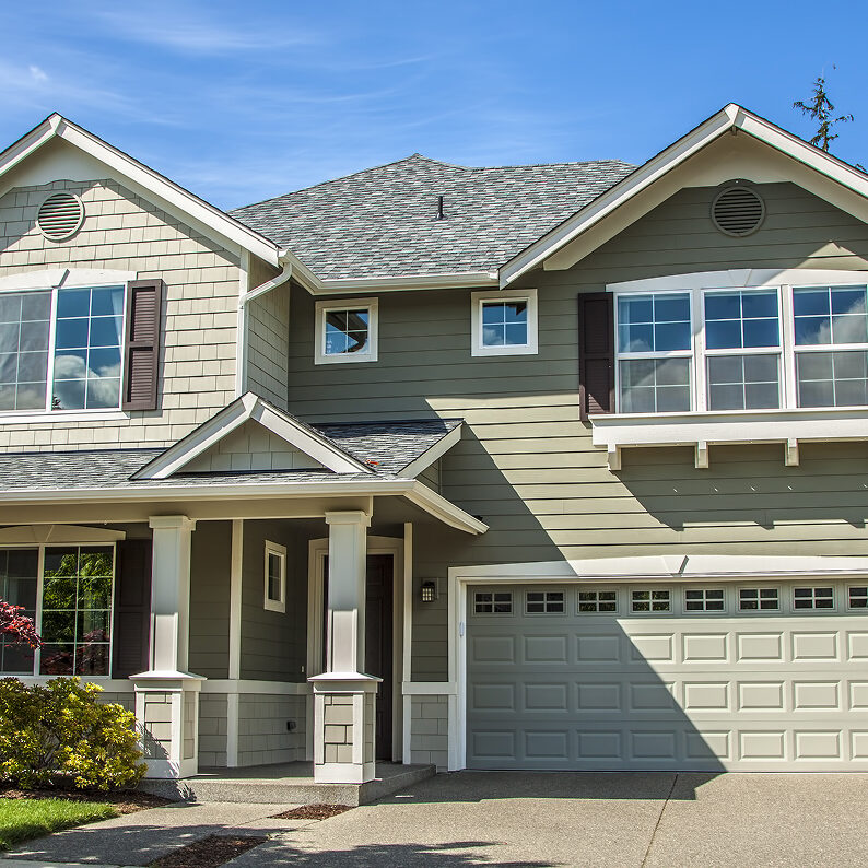 A large house with green siding and a two-car garage. The house has a covered porch and a well-manicured lawn.