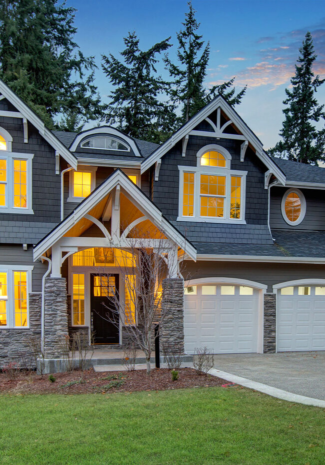 Large house with gray exterior and white trim. The house has a stone porch and three car garage.