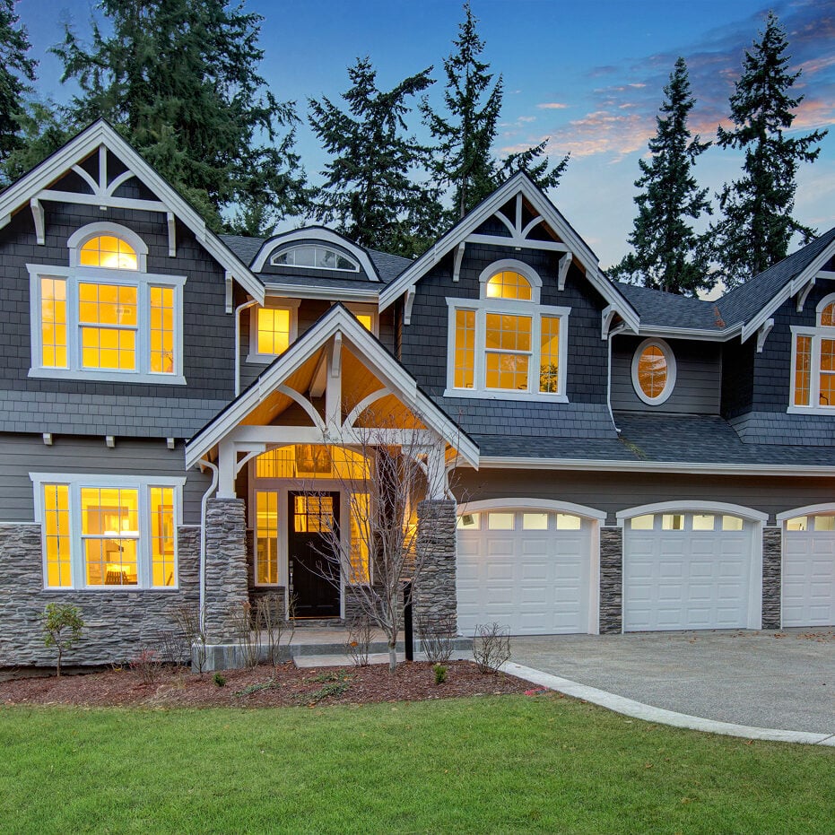 Large house with gray exterior and white trim. The house has a stone porch and three car garage.