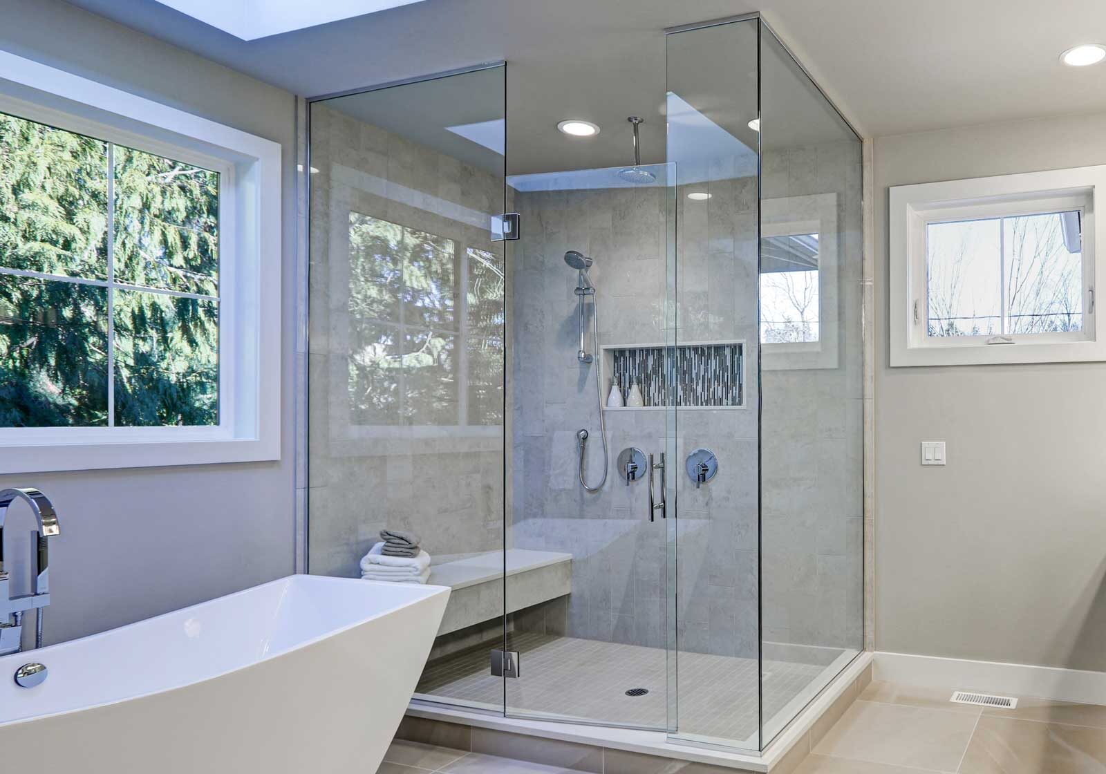 A modern bathroom with a freestanding tub and a glass-enclosed shower. The bathroom features a skylight and large windows.