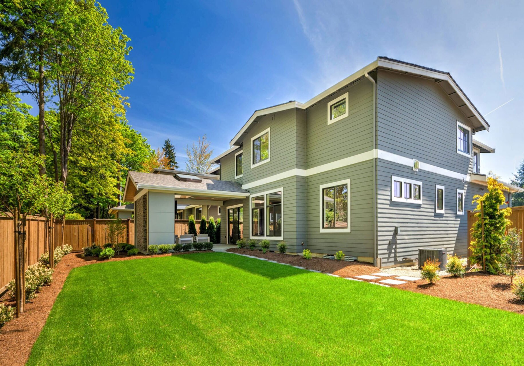 A large two story house with a green lawn and trees. The house has gray siding and white trim.