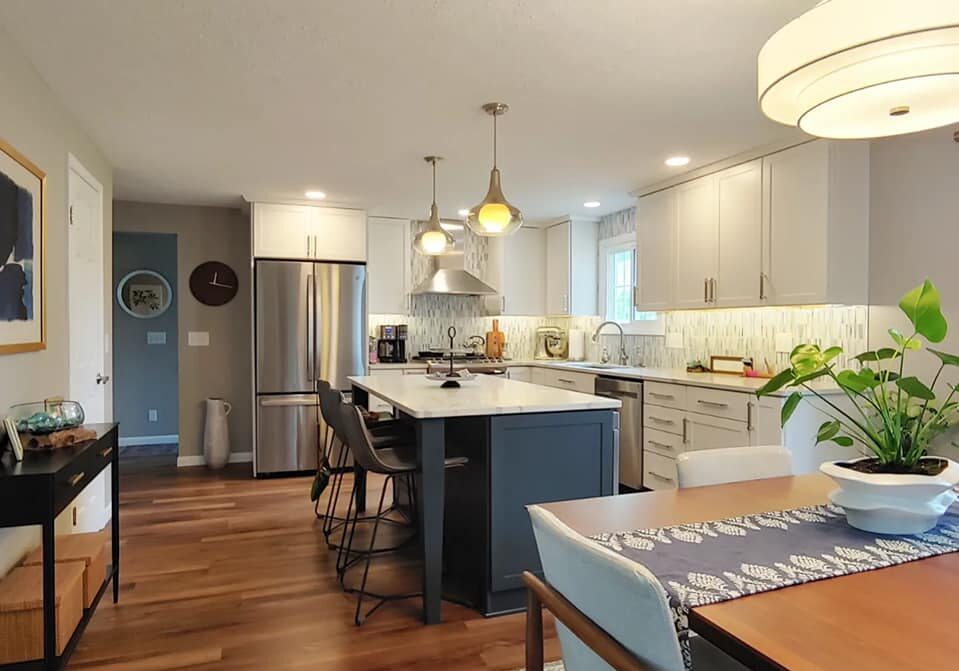 A modern kitchen with white cabinets and a large island. A dining table with chairs is in the foreground.