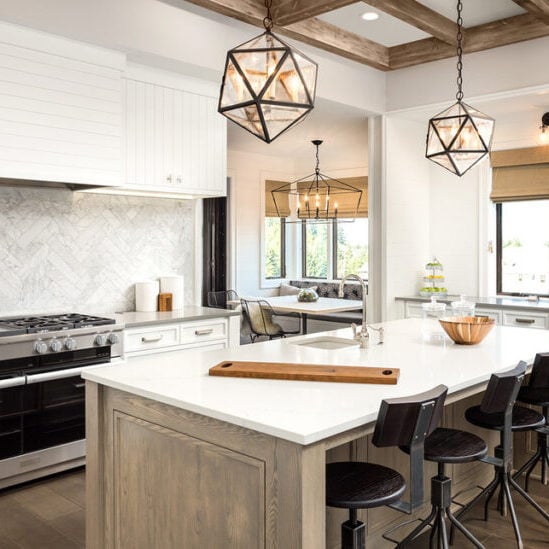 A modern kitchen with white cabinets and a large island. The kitchen features a stainless steel oven and a white countertop.
